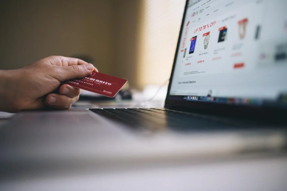 WooCommerce vs PrestaShop: cuál elegir para tu tienda online 9 Persona pagando con una tarjeta de crédito en una tienda online abierta en un portátil, con varios productos en el carrito de compra